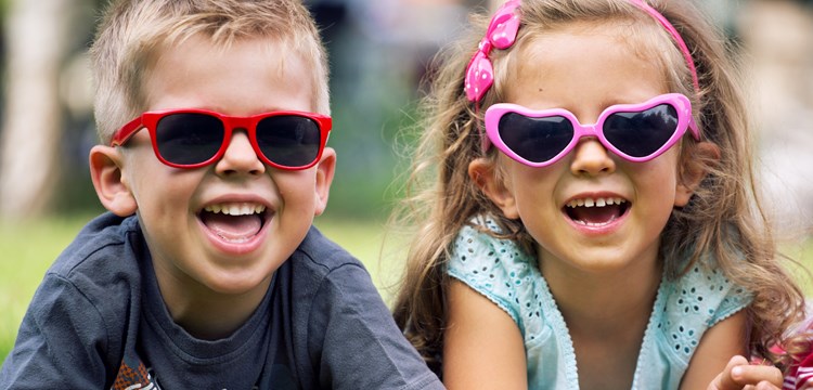 Young boy and girl laying in the grass wearing pink and red sunglasses