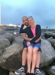 Samantha and Stuart, two foster carers, sat on a rock at the beach while hugging