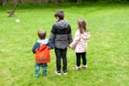 Backs of three children holding hands standing in a garden